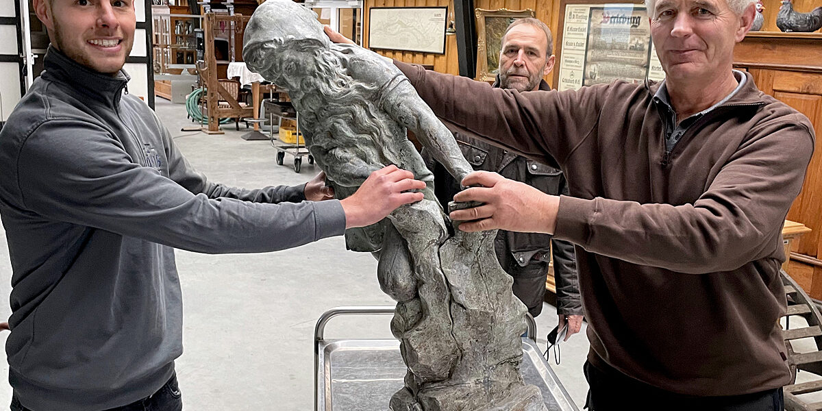 Zum Bild: Metallbauer und Restaurator Felix König (links) übernimmt vom Heimatvereinsvorsitzenden Klaus Daum (rechts) die Brunnenfigur, um sie in seiner Werkstatt in Lüdenscheid genauer unter die Lupe zu nehmen. Im Hintergrund der Finanzexperte und Beirat im Verein, Klaus Sonneborn. (Foto: Heimatverein Landwirtschaft und Brauchtum Bad Berleburg)
